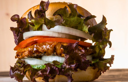 A tall, delicious burger with a toasted bun, layered with a patty, tomato, onion, and vibrant red lettuce.の写真素材