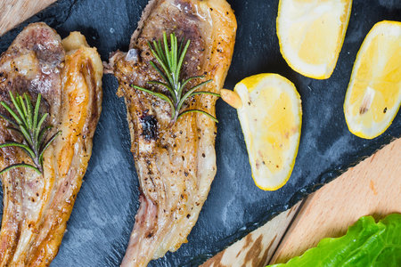 Close-up of perfectly grilled lamb chops seasoned with rosemary, served alongside golden roasted potato wedges and fresh greens.の写真素材