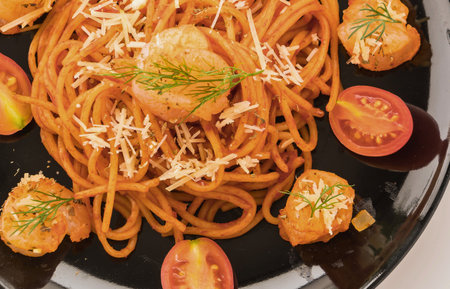 A close-up overhead view of a plate of spaghetti with a rich red sauce, garnished with cheese and herbs, alongside fresh tomato slices and toasted bread.の写真素材