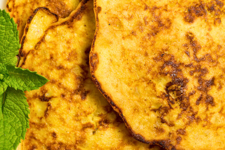 Close-up of crispy, golden-brown zucchini fritters with a sprig of fresh green mint, highlighting their texture and appetizing appearance.の写真素材