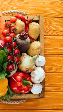 A vibrant assortment of fresh vegetables including beets, potatoes, tomatoes, peppers, and garlic are displayed in a rustic wooden crate.の写真素材