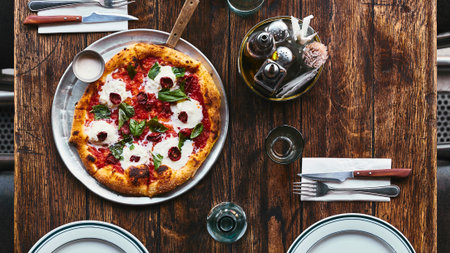 A freshly baked Margherita pizza with melted mozzarella and basil sits on a rustic wooden table, ready to be enjoyed.の写真素材