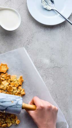 A hand uses a spatula to prepare a sweet, crumbly dessert on parchment paper, ready for plating with a spoon and dish.の写真素材