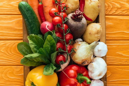 A colorful, overhead view of a wooden crate filled with fresh, raw vegetables including peppers, tomatoes, carrots, and leafy greens.の写真素材