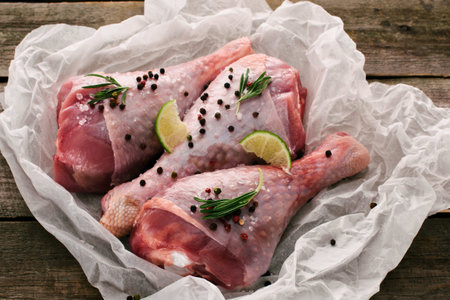 Three raw turkey legs are seasoned with fresh rosemary sprigs, peppercorns, and lemon slices, presented on crumpled parchment paper.の写真素材