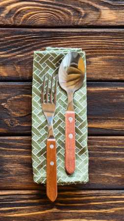 A fork and spoon with wooden handles rest on a textured green napkin, set against a warm, dark wooden background.の写真素材