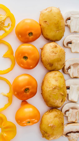 A vibrant arrangement of yellow bell pepper rings, cherry tomatoes, potatoes, and sliced mushrooms, ready for cooking.の写真素材