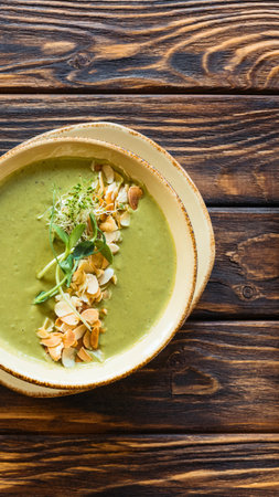 A vibrant green soup served in a shallow bowl, garnished with fresh herbs and a crunchy topping, presented on a wooden surface.の写真素材