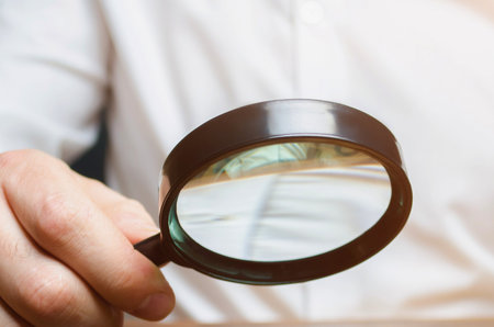 A person holds a magnifying glass, focusing on small text, suggesting detailed inspection or research.の写真素材