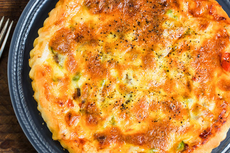 A close-up overhead view of a delicious, golden-brown savory tart filled with visible vegetables and herbs, presented on a dark platter.の写真素材