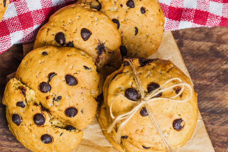 A close-up overhead view of several freshly baked chocolate chip cookies, some tied together with rustic twine, on a wooden surface.の写真素材