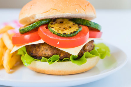 A close-up shot of a juicy burger with lettuce, tomato, cheese, and grilled zucchini, served with crispy french fries.の写真素材