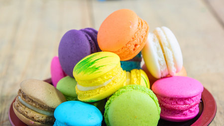 A vibrant pile of assorted French macarons in various bright colors, presented in a rustic bowl on a wooden surface.の写真素材