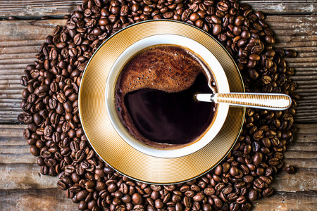 A top-down view of a steaming cup of dark coffee, nestled within a circle of roasted coffee beans on a rustic wooden surface.の写真素材