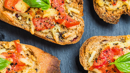 Close-up view of toasted bread slices generously topped with chopped tomatoes, melted cheese, and fresh basil leaves.の写真素材
