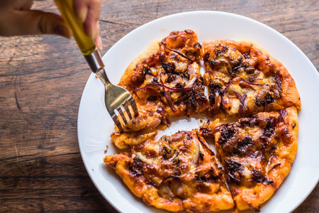 A close-up shot of a golden-brown pizza on a white plate, with a fork lifting a cheesy slice.の写真素材