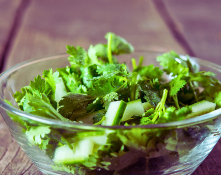 A close-up shot of vibrant green chopped cilantro leaves and stems in a transparent glass bowl, set against a rustic wooden background.の写真素材