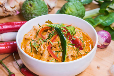 A close-up of a flavorful Thai red curry dish, garnished with fresh herbs and served with vibrant red chilies and onions.の写真素材