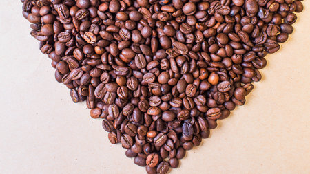 A close-up overhead view of numerous dark brown roasted coffee beans artfully arranged into a heart shape against a neutral, light-colored surface.の写真素材