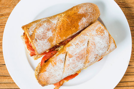 A close-up overhead view of a halved ciabatta sandwich on a white plate, showcasing its savory fillings.の写真素材