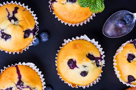 A close-up overhead view of golden-brown blueberry muffins in paper liners, garnished with fresh mint and a spoon.の写真素材