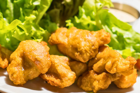 A close-up shot of delicious, golden-brown chicken nuggets piled high next to a vibrant green lettuce salad.の写真素材