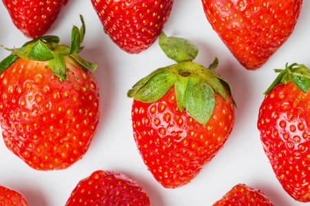 A close-up, overhead view of vibrant red strawberries with green stems, showcasing their textured skin and seeds.の写真素材