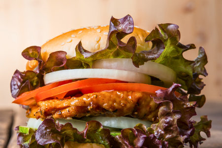 A close-up, mouthwatering shot of a tall, layered burger with fresh vegetables and a golden bun, presented on a wooden surface.の写真素材