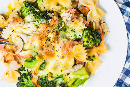 A close-up shot of a creamy pasta dish featuring bow-tie pasta, vibrant broccoli florets, and succulent shrimp, topped with melted cheese.の写真素材