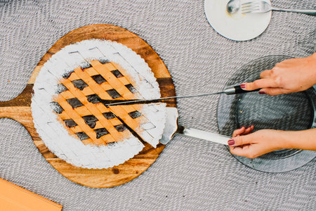 Two hands are shown using knives to cut slices from a delicious pie with a golden brown lattice crust, ready to be served.の写真素材
