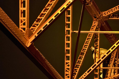 Close-up view of the complex, geometric patterns of illuminated orange steel bridge trusses against a dark night sky.の写真素材