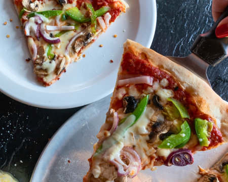 Two generous slices of vegetarian pizza are presented on white plates, showcasing colorful bell peppers, onions, and mushrooms.の写真素材