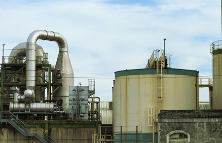 A large industrial complex featuring prominent storage tanks and intricate networks of metal pipes and machinery under a cloudy sky.の写真素材