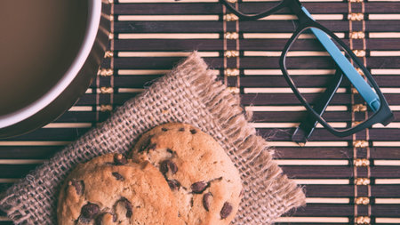 A warm cup of coffee, a delicious pastry, and reading glasses are arranged on a bamboo mat for a relaxing morning.の写真素材