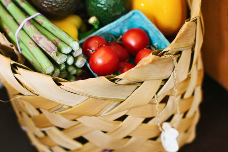 A woven basket overflowing with vibrant fresh vegetables including asparagus, cherry tomatoes, and a...