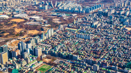 An expansive aerial perspective showcases a sprawling city with numerous high-rise buildings and interspersed green spaces like parks and sports fields.の写真素材