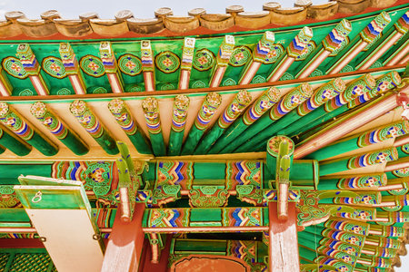 A close-up view of the elaborately decorated eaves and ceiling of a traditional Korean palace building, showcasing vibrant colors and detailed craftsmanship.の写真素材