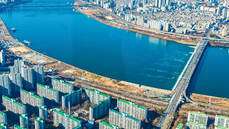 An elevated perspective showcases a broad blue river bisecting a densely populated urban landscape with numerous buildings and a prominent bridge.の写真素材