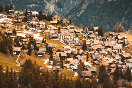 An aerial view showcases a dense collection of traditional wooden chalets and houses built on a steep, forested mountainside.の写真素材