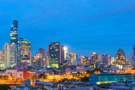 A sprawling city skyline at twilight, with numerous buildings and skyscrapers brightly lit against a deep blue sky.の写真素材