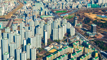 An expansive aerial perspective showcases a densely packed city with numerous high-rise apartment buildings and interspersed green park areas.の写真素材