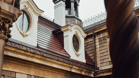 Close-up view of a historic European building's facade, showcasing intricate architectural details like dormer windows and a distant tower.の写真素材