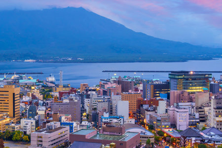 A vibrant city lights up at dusk with a large mountain and body of water in the background.の写真素材