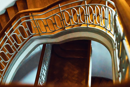 A close-up view of a vintage, curved staircase featuring an ornate metal railing and a dark wooden door below.の写真素材