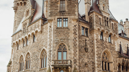 Close-up view of a weathered stone castle tower showcasing intricate Gothic architectural details and arched windows.の写真素材