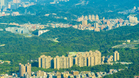 A high-angle view showcases a sprawling urban environment nestled against a backdrop of densely forested mountains, with numerous residential buildings.の写真素材