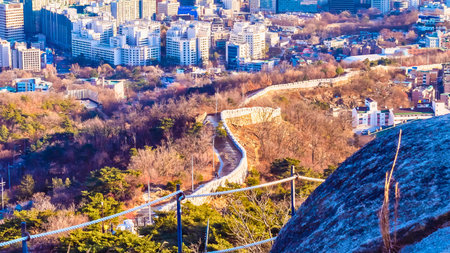 A vibrant cityscape unfolds with buildings nestled amongst rolling hills and lush trees under a bright sky.の写真素材