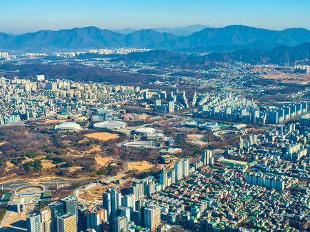 A sprawling city with numerous buildings, parks, and distant mountains under a clear blue sky.の写真素材