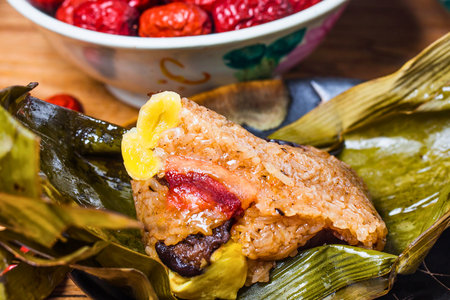 A close-up of a savory sticky rice dumpling, revealing its filling of red dates and other ingredients, wrapped in green leaves.の写真素材