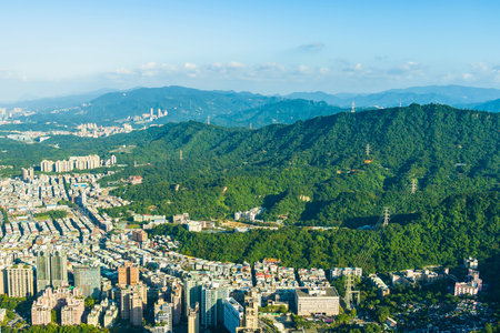 An expansive aerial perspective shows a dense urban landscape transitioning into rolling, verdant mountains under a clear, bright sky.の写真素材